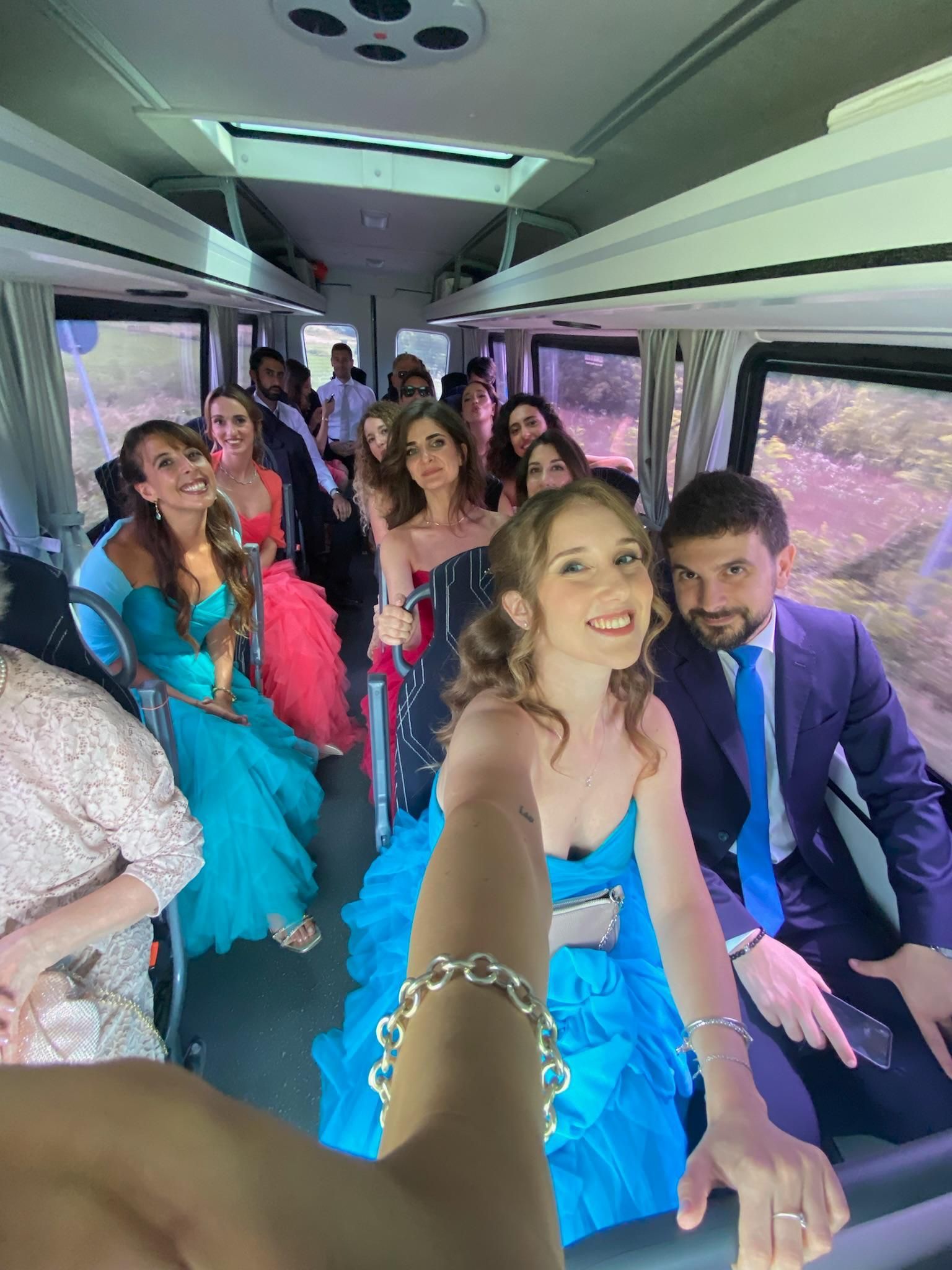 People in formal attire smiling inside a decorated bus, with blue and pink decor.