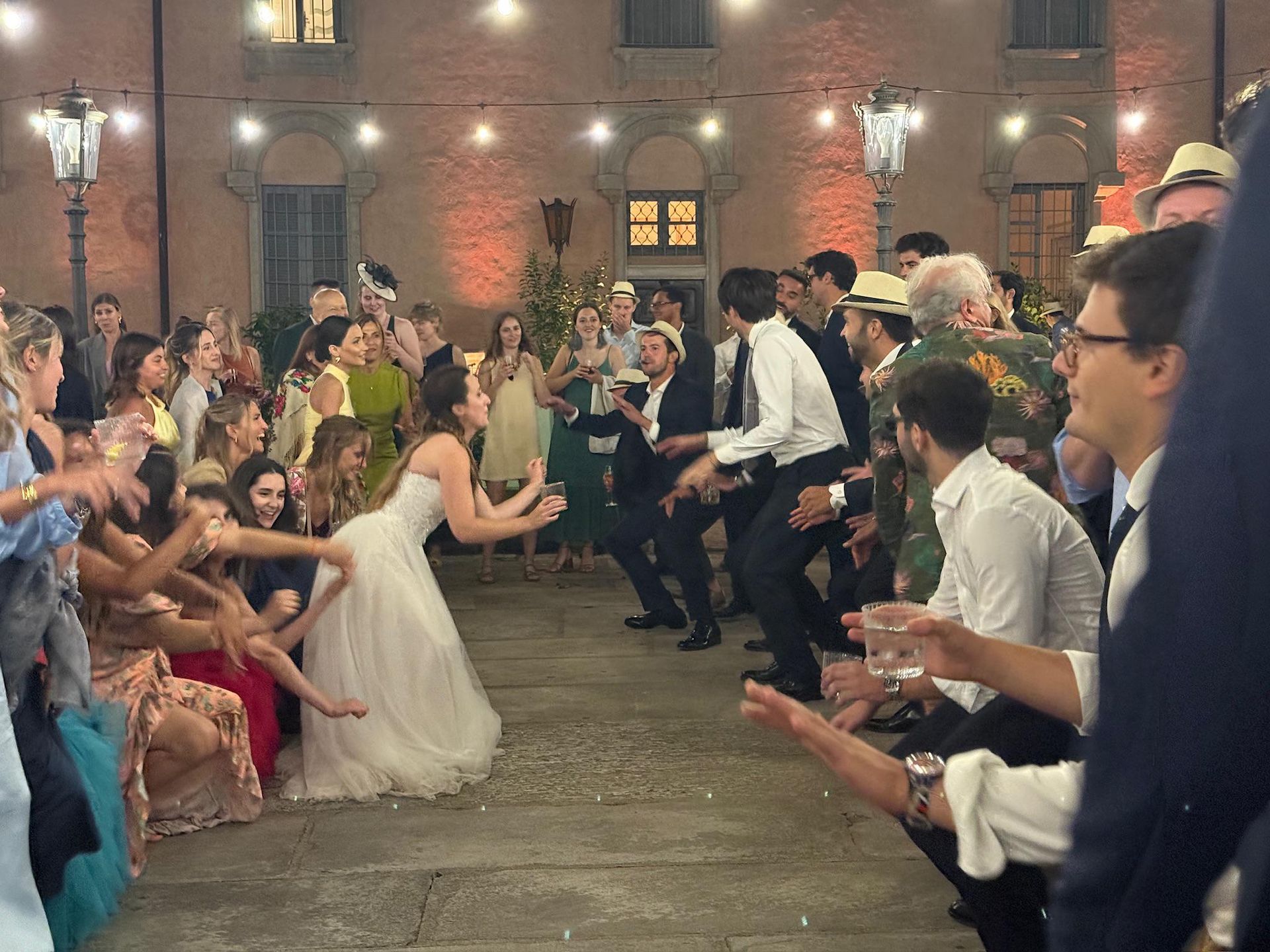 Wedding guests clap as the bride dances in a courtyard at night.
