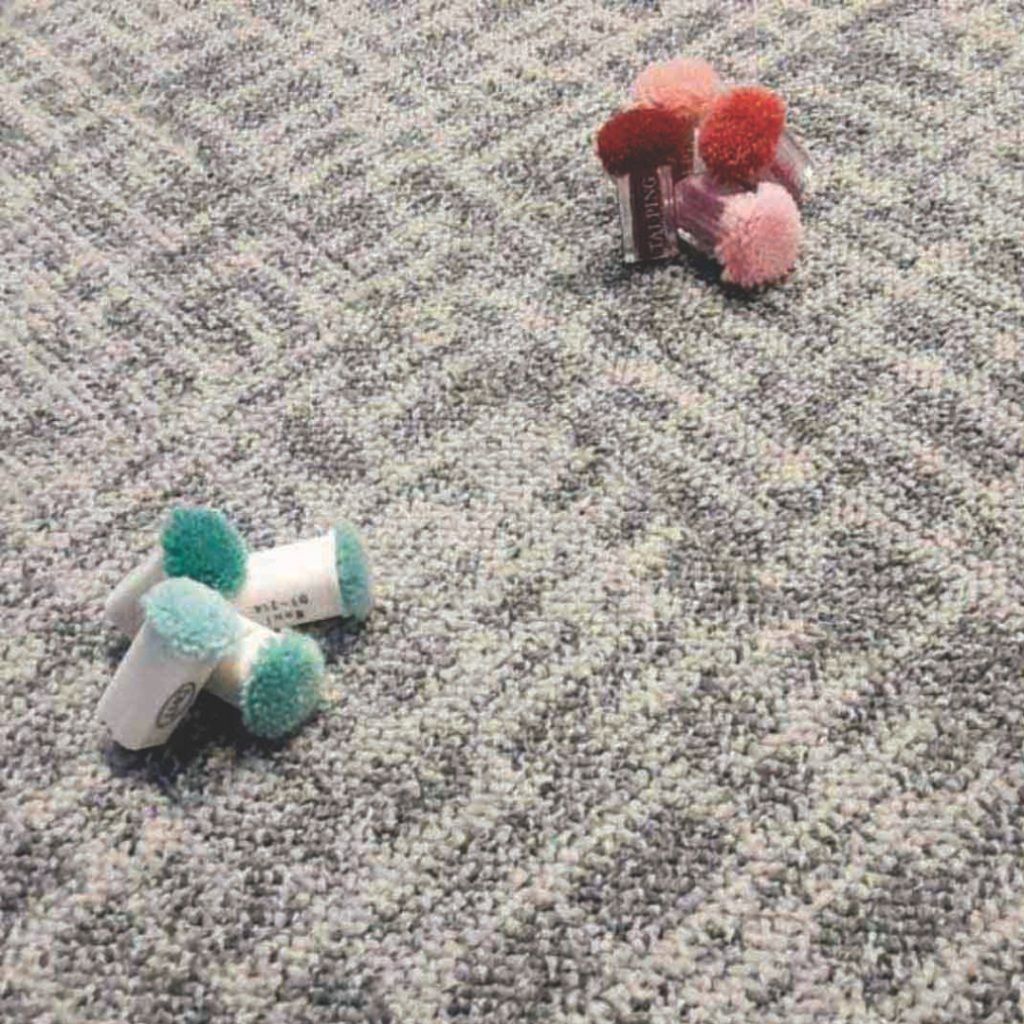 Pequeños adornos de pompones en color turquesa y rosa sobre una alfombra gris.