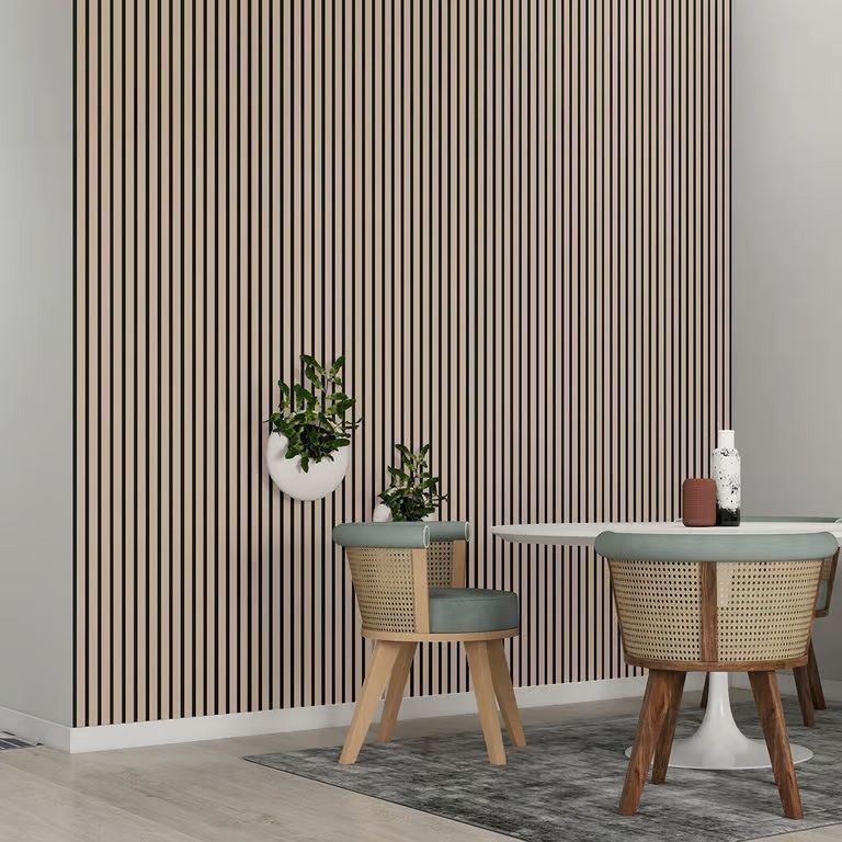 Rincón de comedor moderno con pared a rayas, mesa pequeña y dos sillas de mimbre sobre una alfombra gris.