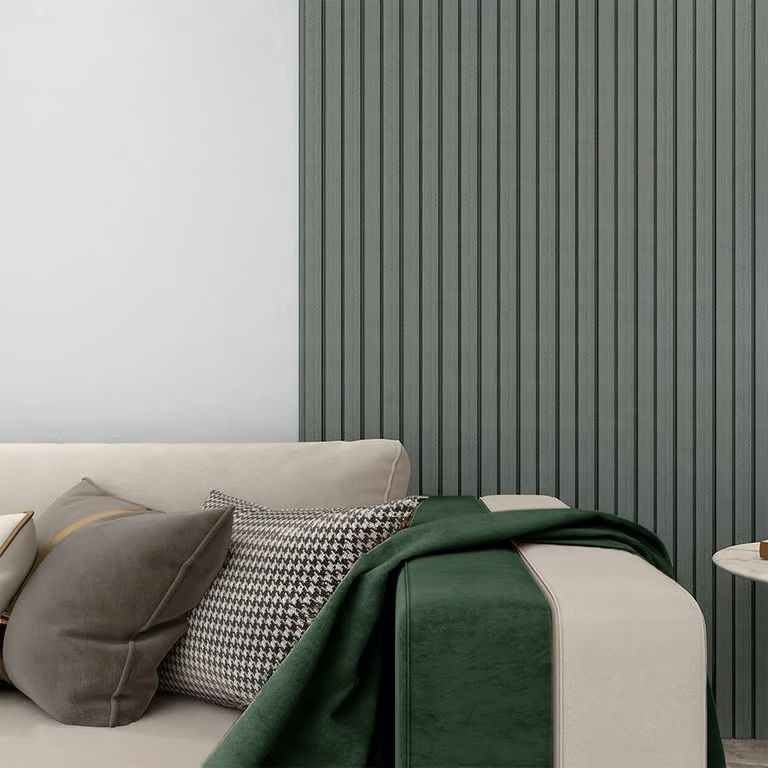 Rincón de sala de estar moderno con sofá beige, manta verde, cojines estampados y paneles de pared verticales grises.
