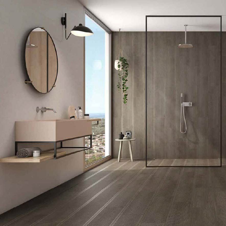 Baño minimalista en color gris con tocador flotante, espejo ovalado, ducha a ras de suelo y luz natural.