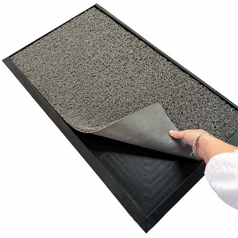 Levantando con la mano una esquina de una alfombrilla gris moteada, se descubre un reverso negro debajo.