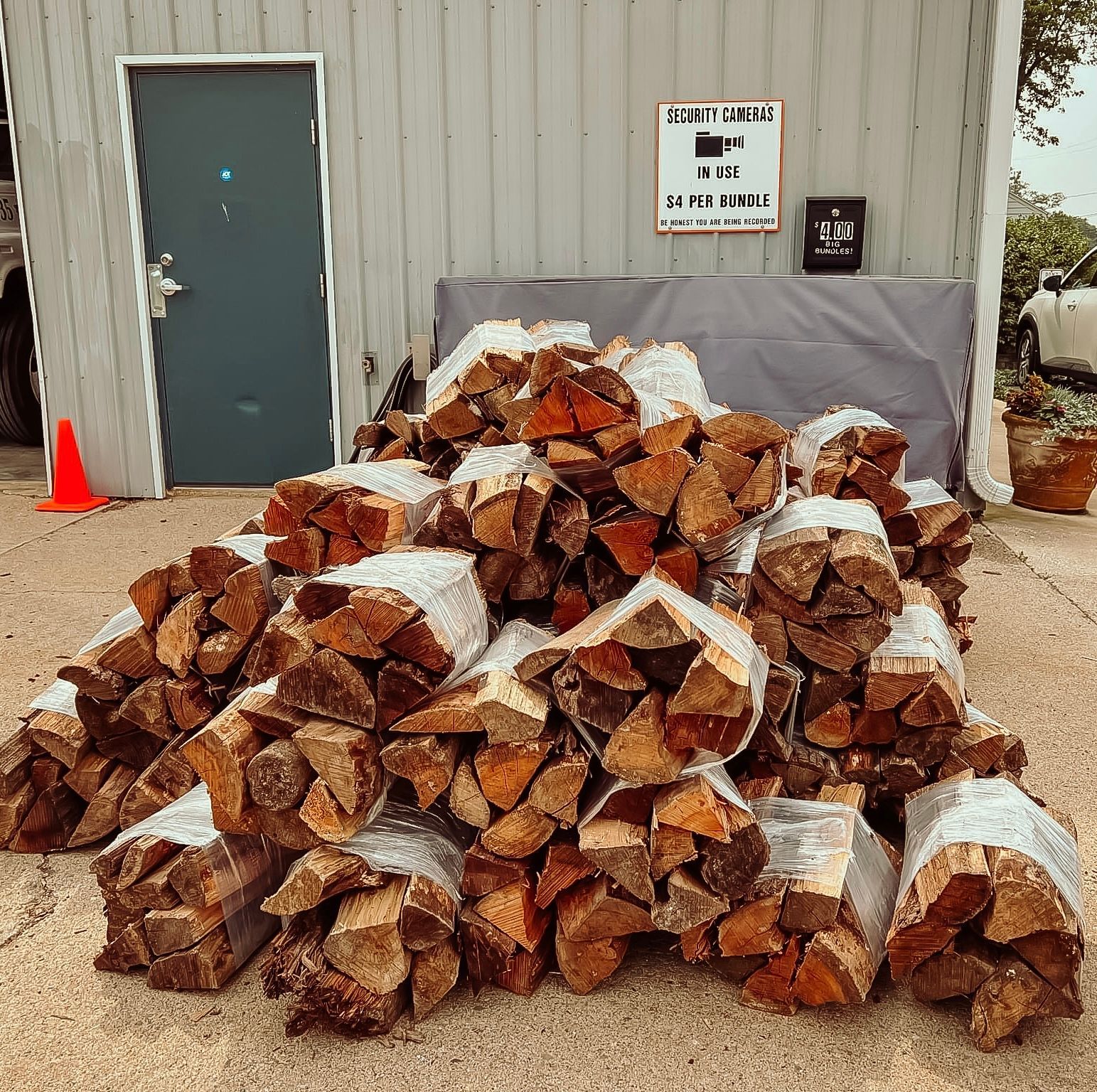 Bundles of firewood stacked outside a building with a gray door and sign.