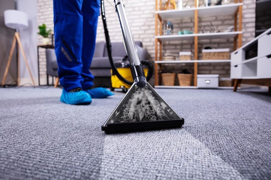 Carpet cleaner vacuuming a gray rug in a living room with blue pants and blue shoes visible