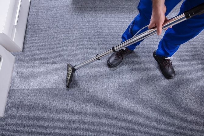 Person using a carpet cleaner on a gray carpet indoors
