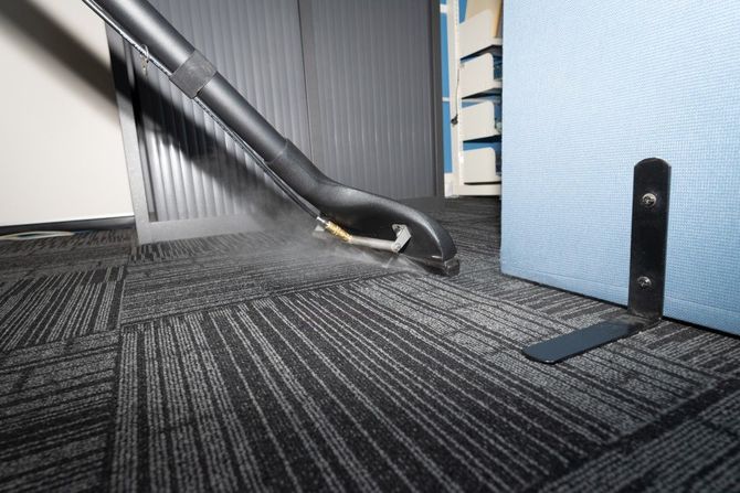 Black vacuum hose on carpet beside a wall and blue partition in an office-like room