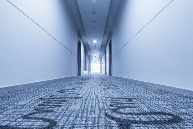Empty modern office hallway with blue carpet and bright lights at the far end