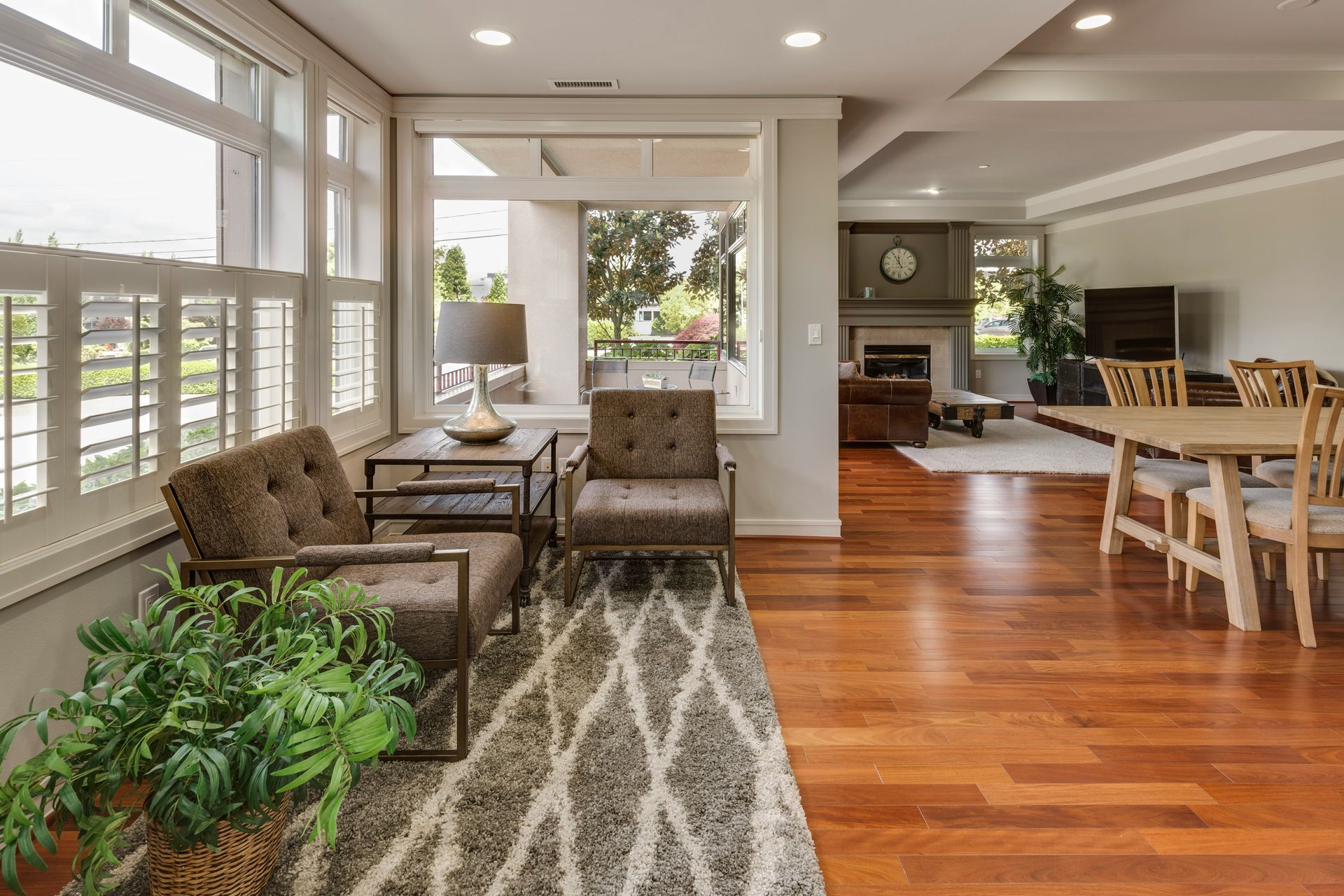 Bright open living room with tufted chairs, patterned rug, hardwood floors, and dining area by large windows