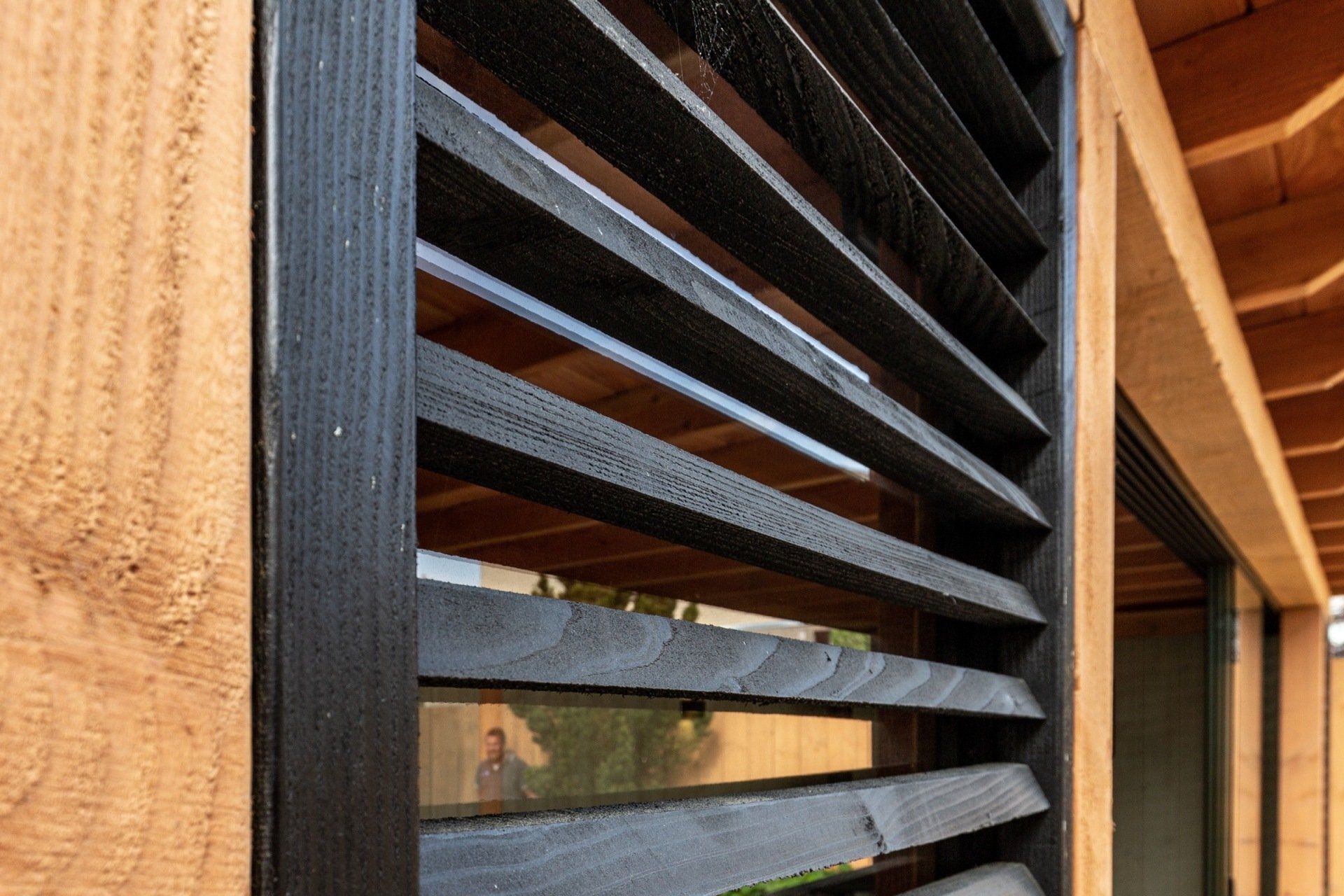 Detailopname van zwarte, houten lamellenluiken tegen een warmgetinte, natuurlijke houten constructie.