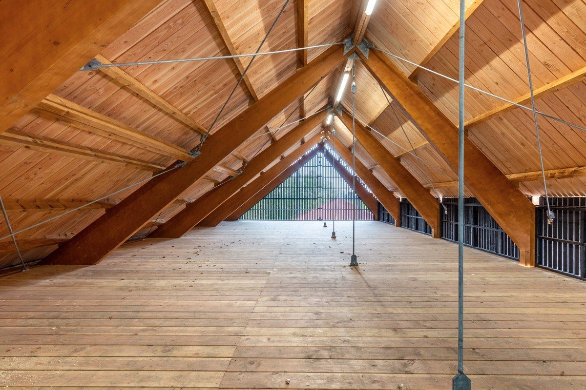Een ruime, lege zolder met zichtbare houten balken, gewelfde plafonds en een lichtgekleurde houten vloer.