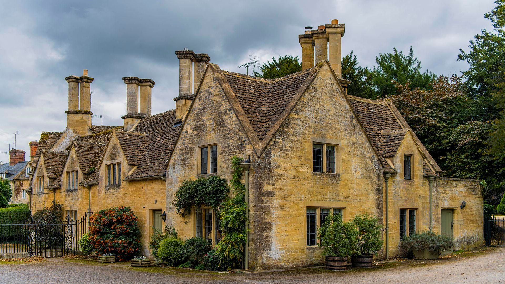 a large cotswold stone house with a roof and chimneys on a cloudy day .
