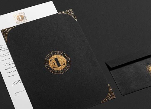 a black letterhead with a gold logo on it is sitting on top of a black envelope .