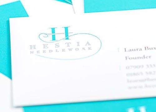 A business card for hestia needlework with a blue background