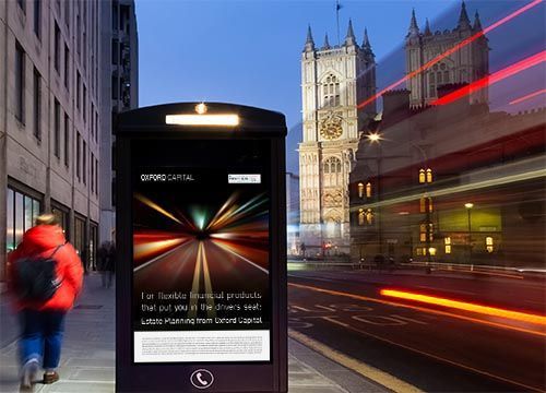 a man in a red jacket is walking down a street next to a bus stop with an adshel advertisement for oxford capital.