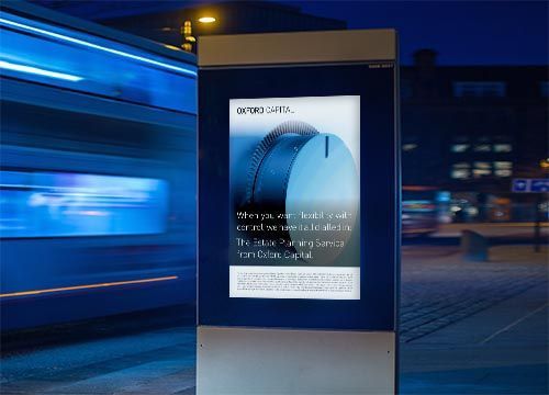 an adshel billboard on the side of a bus stop at night with an advertisement for oxford capital.
