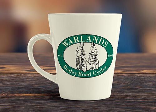 a white coffee mug with a green warlands logo on it is sitting on a wooden table .