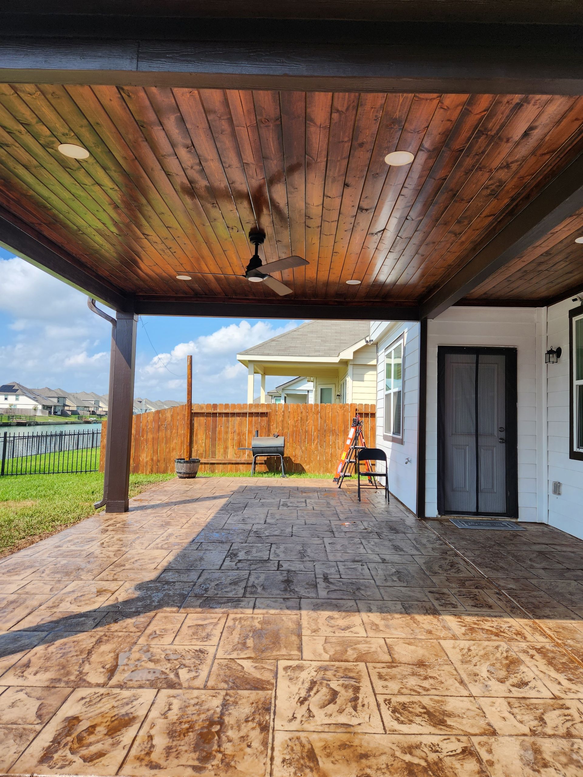 A covered patio with chairs and a ceiling fan next to a pool.