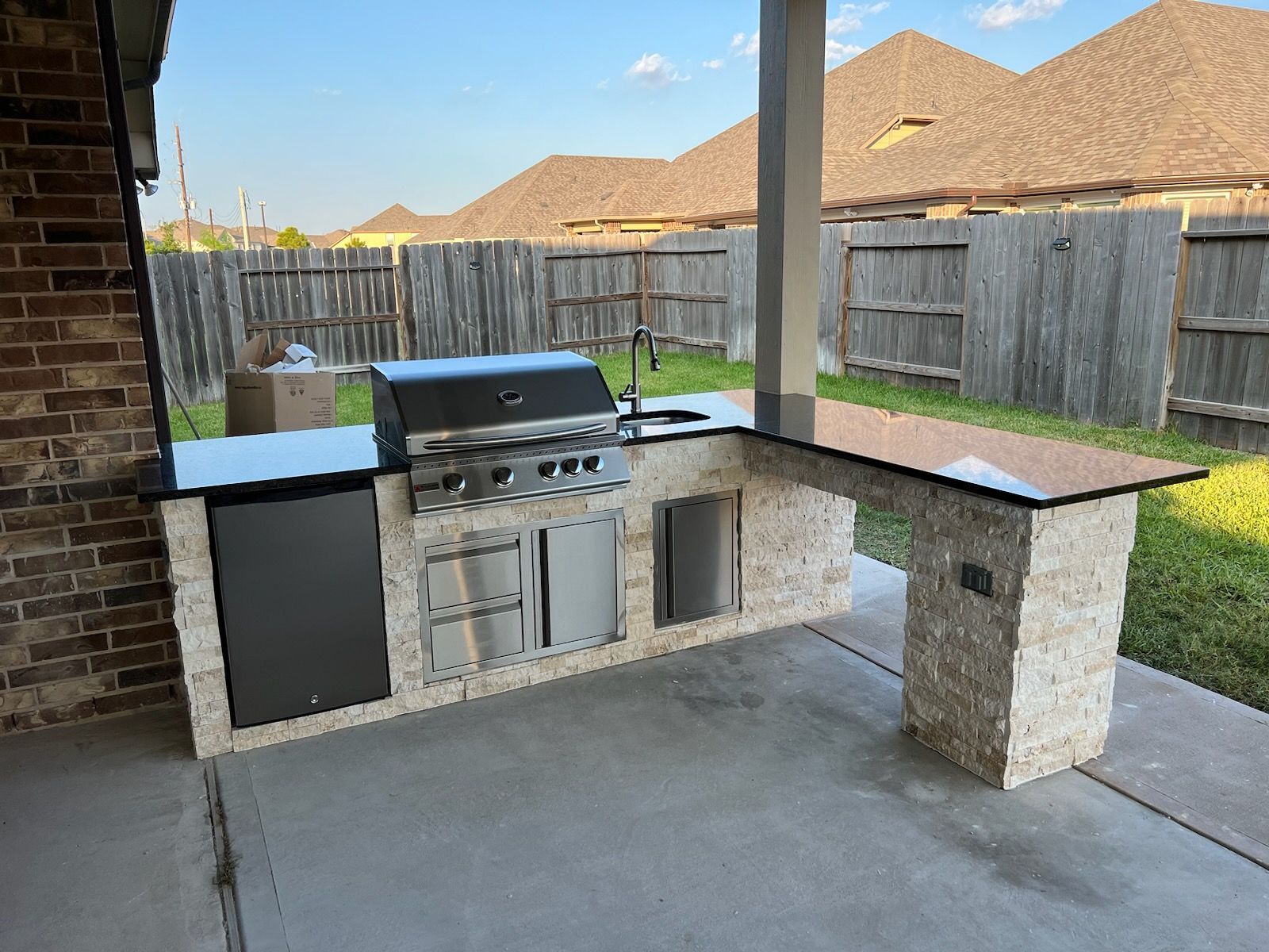 An outdoor kitchen with a grill , sink , and fence in the background.