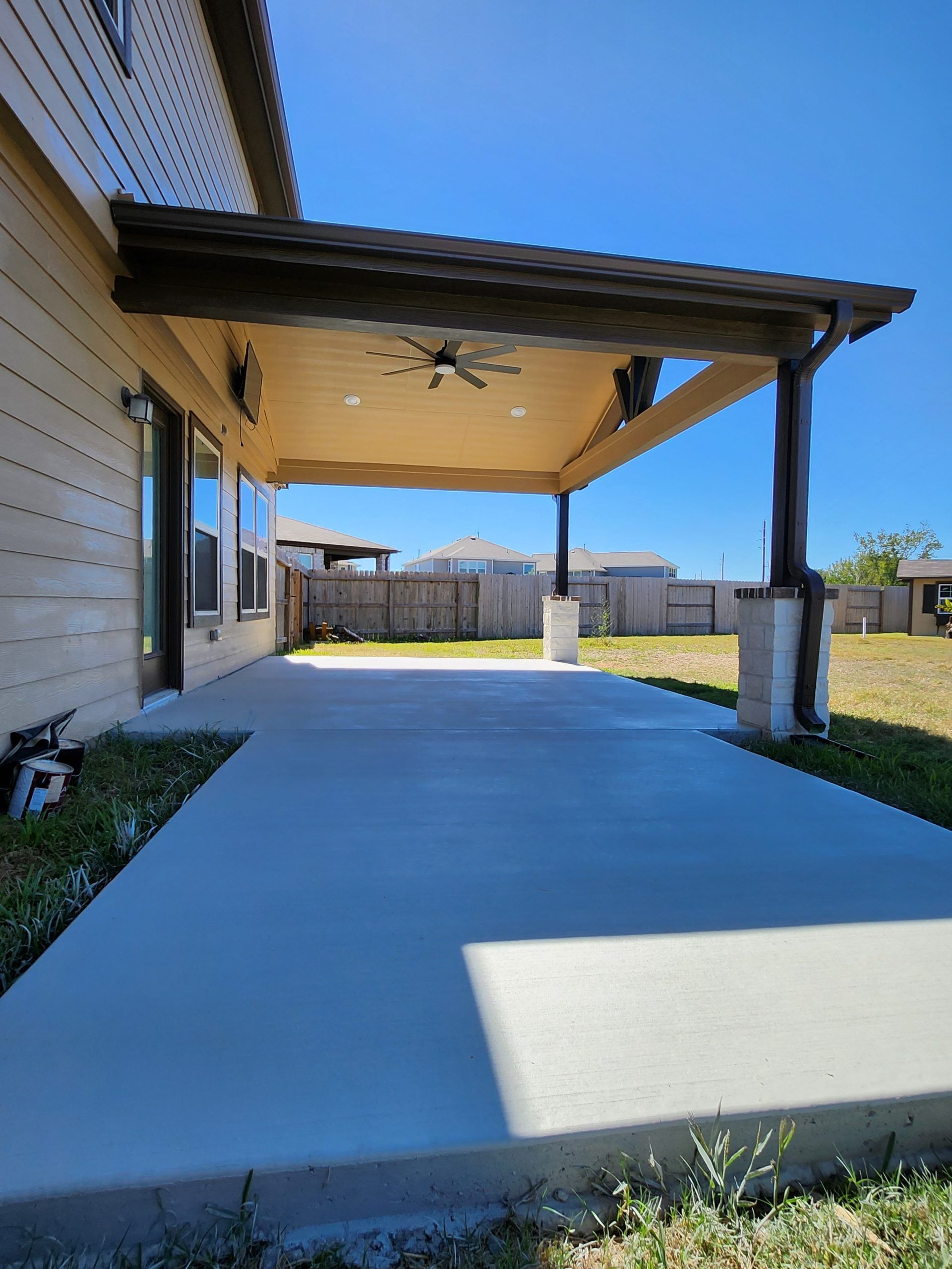 A covered patio with a ceiling fan in the backyard of a house.