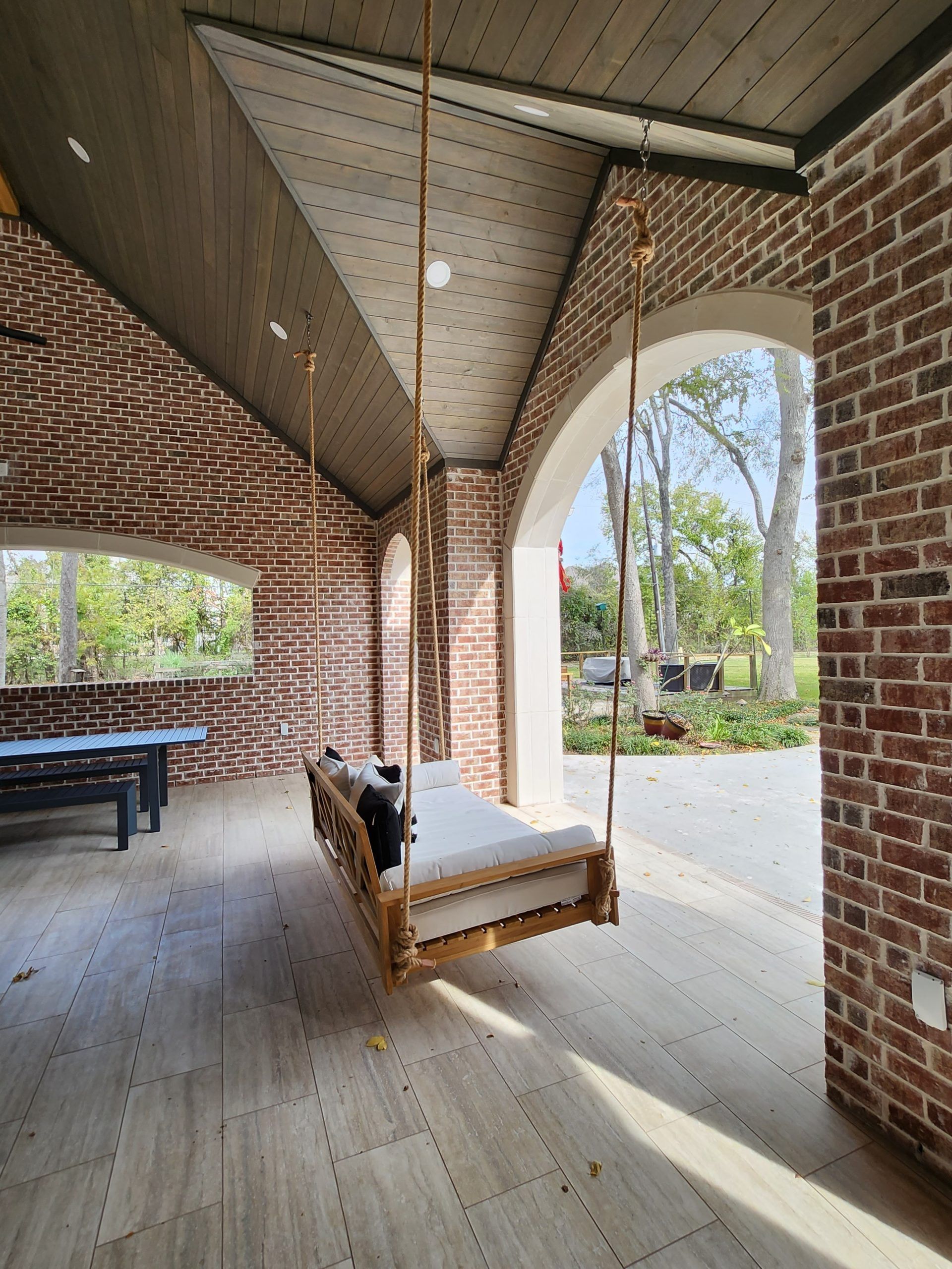 A wooden swing is hanging from the ceiling in a room with brick walls.