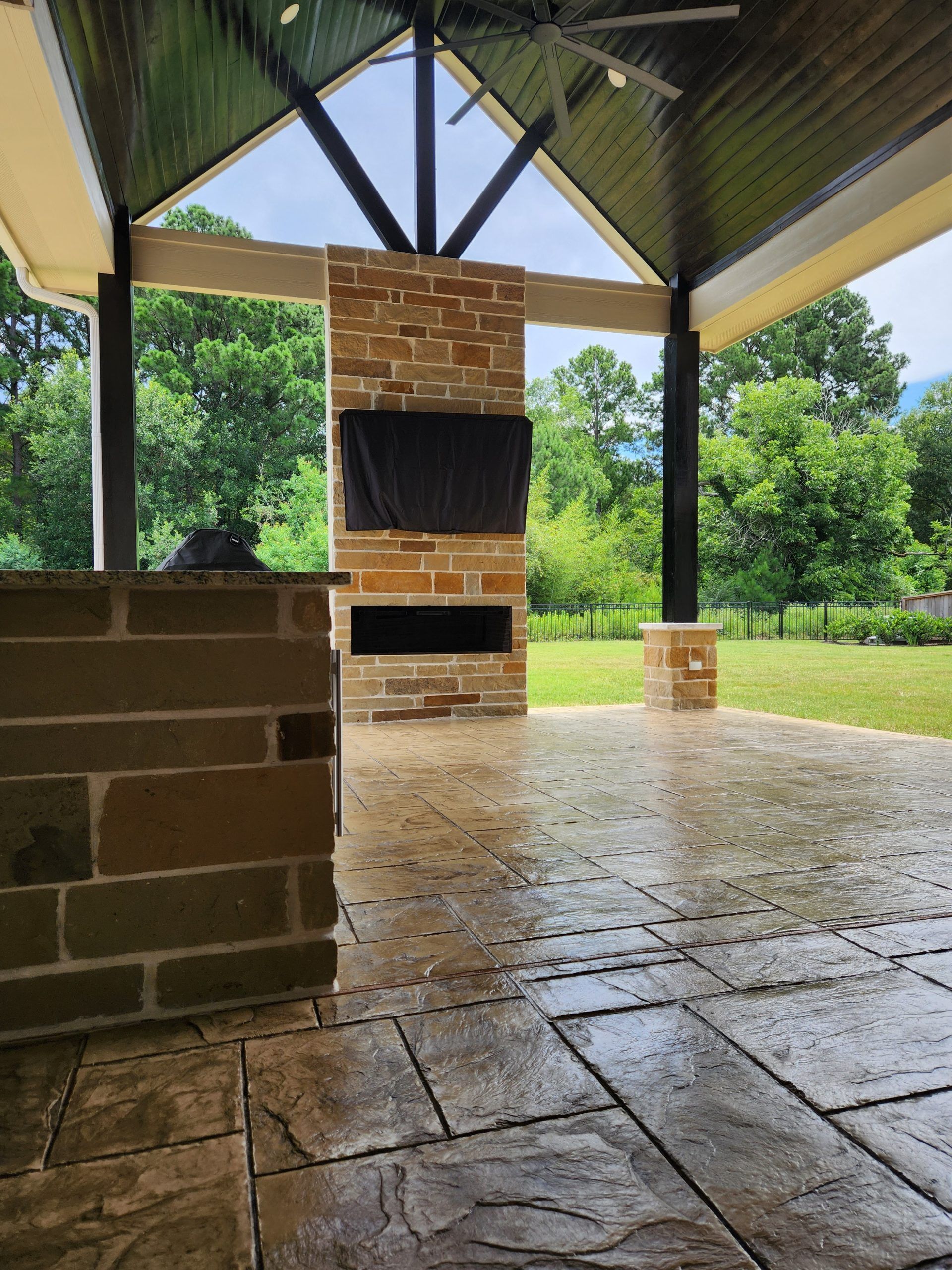A patio with a stone fireplace and a flat screen tv.
