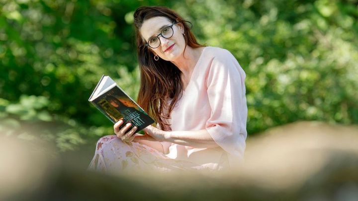 Vrouw leest een boek in een zonnige, groene tuin.