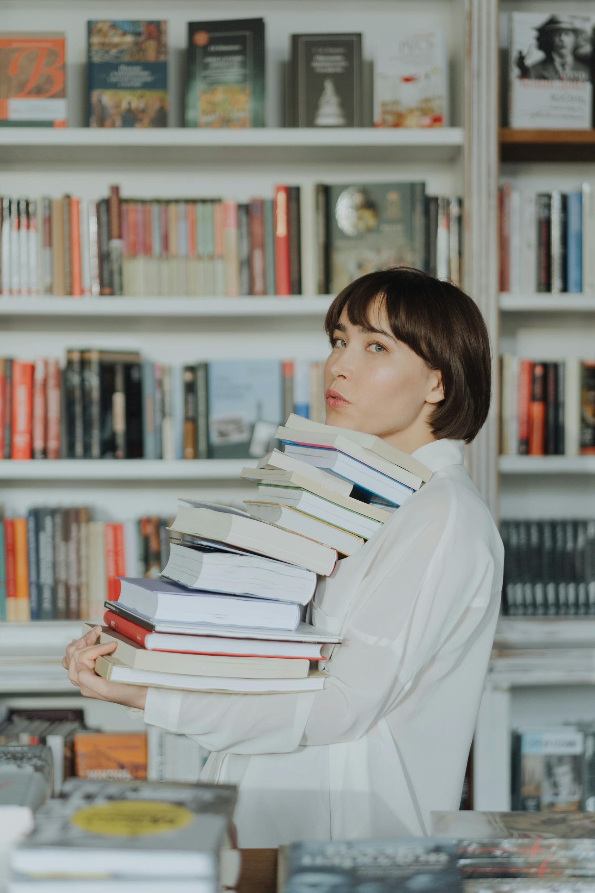 Persoon in een wit shirt die een stapel boeken vasthoudt voor boekenplanken in een bibliotheek