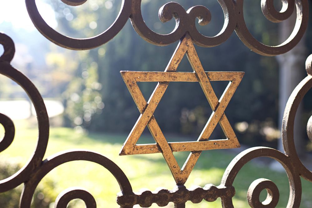 A gold Star of David set in ornate ironwork, blurred green foliage in the background.