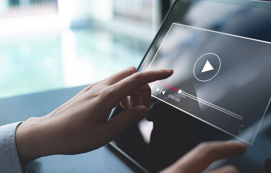 Person's hand touching a tablet screen with a video player interface; progress bar and play button visible.