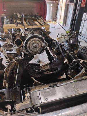 A disassembled vehicle chassis with parts scattered in a workshop setting.