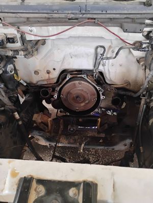 Engine bay of a vehicle with components visible. The area appears dirty with dark stains, some wires, and metal parts.
