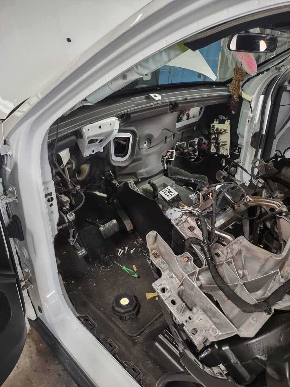 Interior of a white car, dashboard disassembled, wires and components exposed.