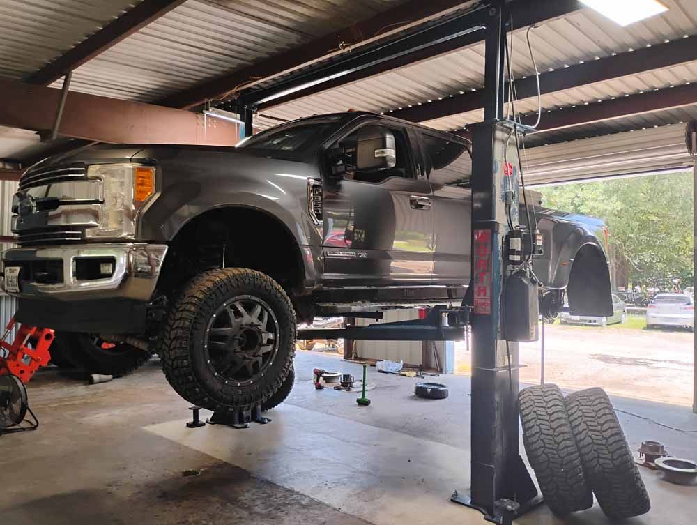 A grey pickup truck raised on a lift inside a repair shop.