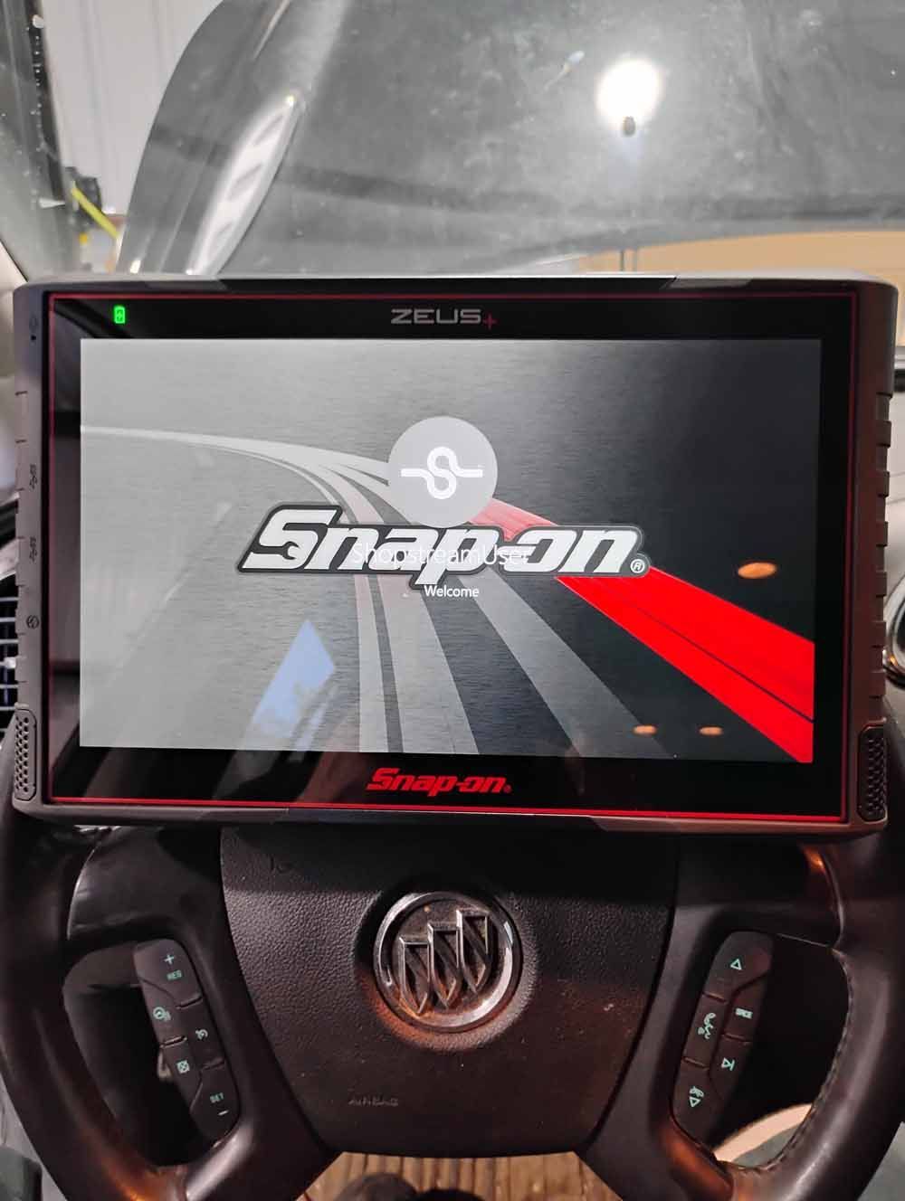 Snap-on diagnostic tool on car's steering wheel, powered on, with Snap-on logo.