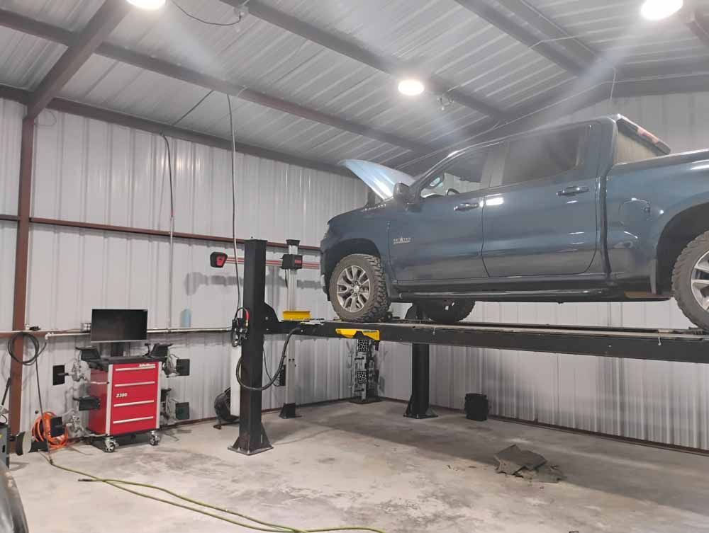 A pickup truck is raised on a lift inside a garage; alignment equipment is nearby.