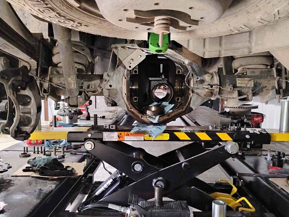 Underside of a vehicle, rear axle open on a lift, repair in progress, tools around.