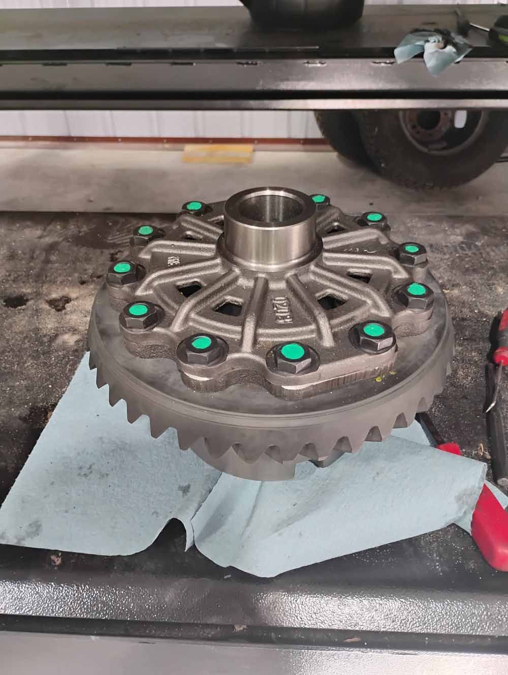 Differential gear assembly with green bolts on a workbench.