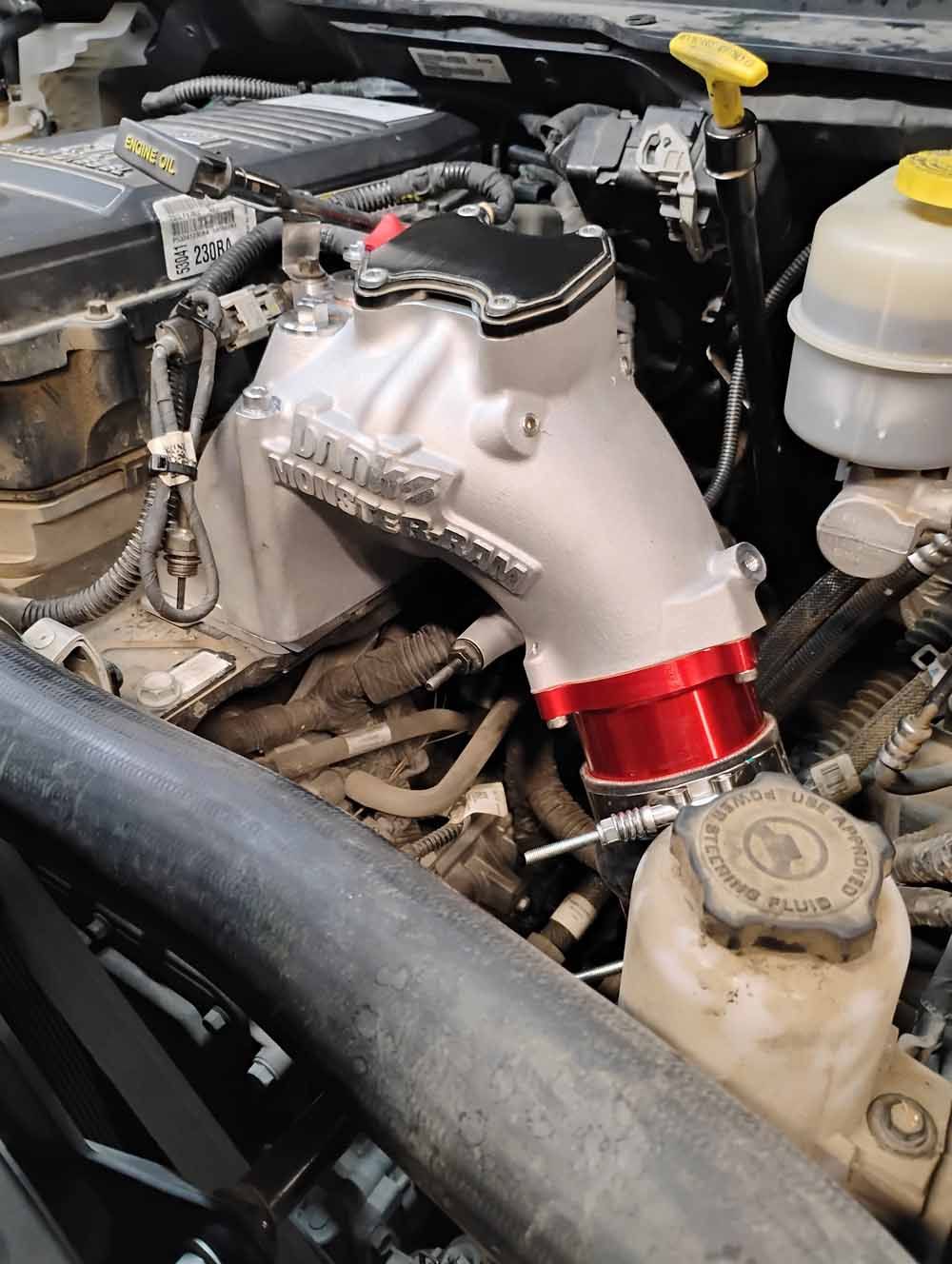 Engine bay with a silver and red intake component installed on a Dodge Ram truck.