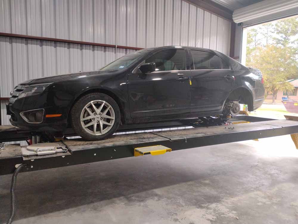Black car on a hydraulic lift inside a garage. One wheel removed.
