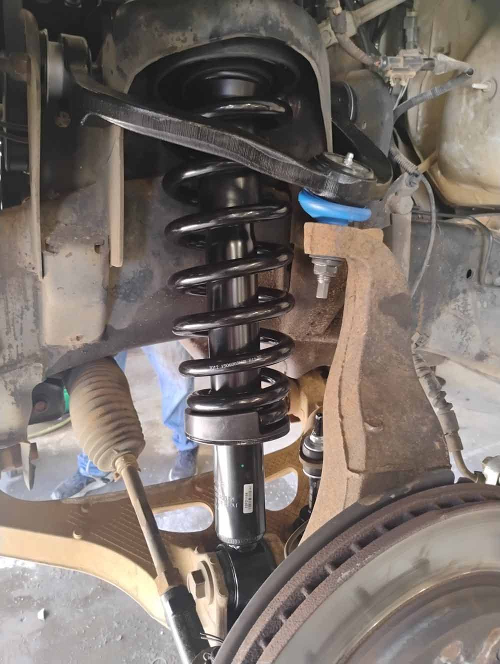Vehicle suspension system with coil spring and shock absorber visible. Black and metal components.