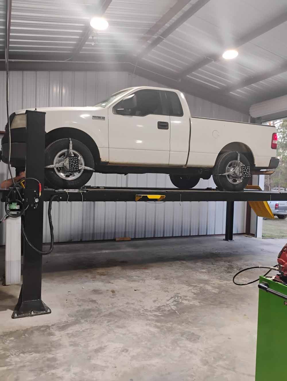 White pickup truck on a four-post car lift inside a garage. Alignment equipment attached to the wheels.