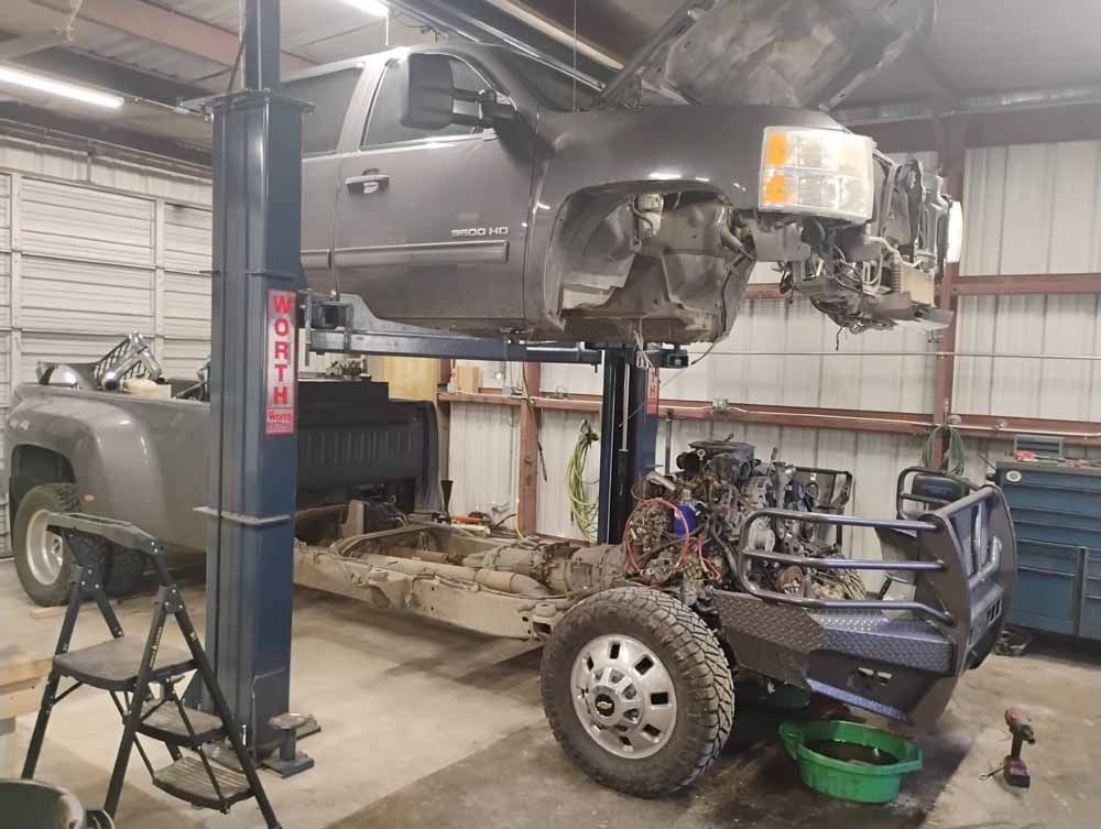 A truck cab on a lift, separated from its frame and engine, in a shop.