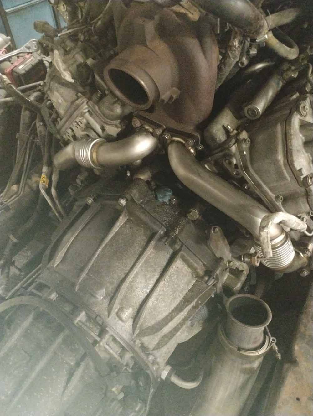 Close-up of a truck engine with a turbocharger and exhaust piping. The engine is grey and has multiple tubes and wires attached.