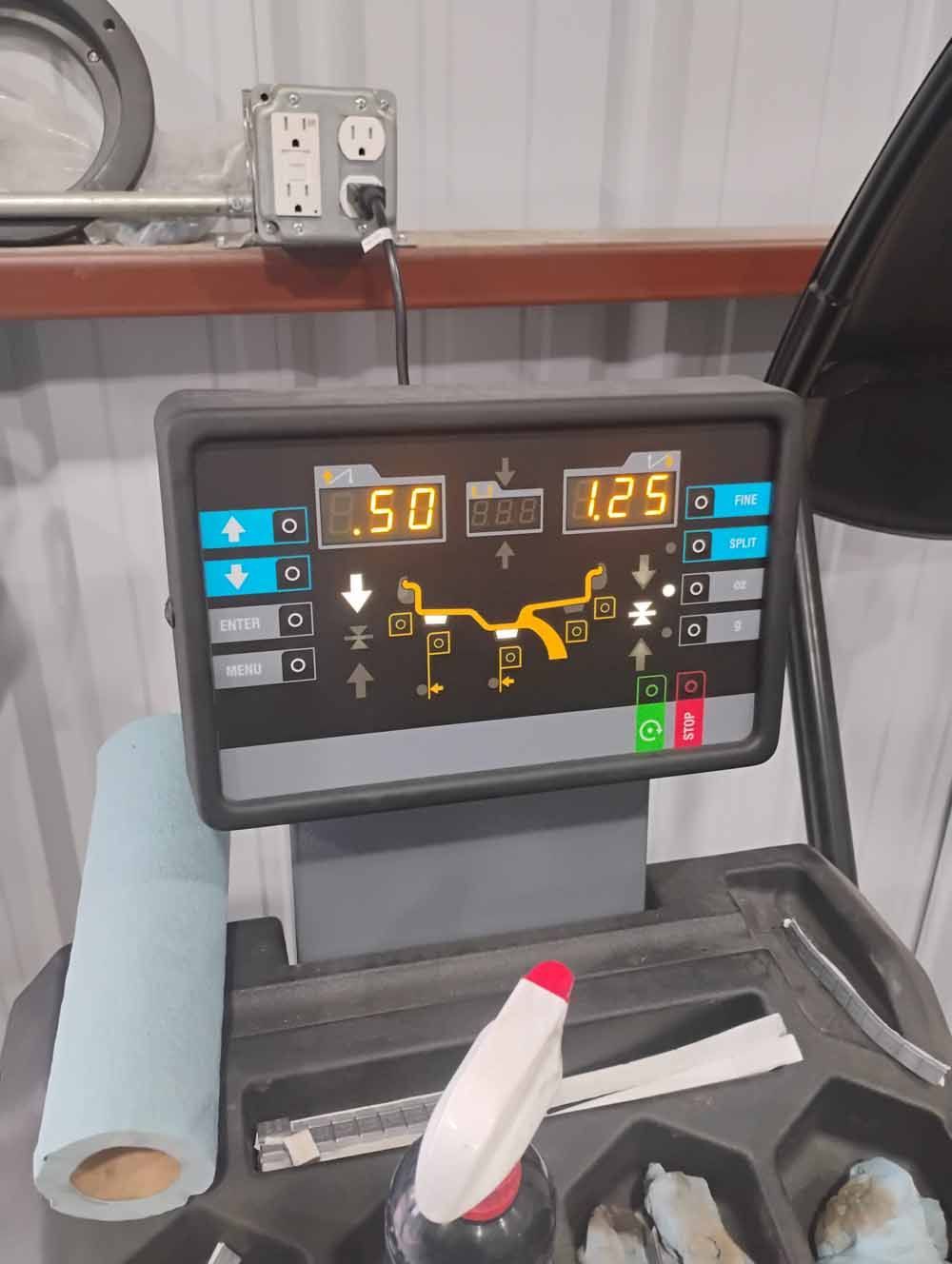 Wheel balancing machine screen displaying weight readings and wheel diagram. A spray bottle and paper towel roll are in the foreground.