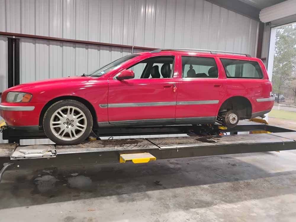 Red Volvo wagon on a car lift inside a garage, missing a front wheel.