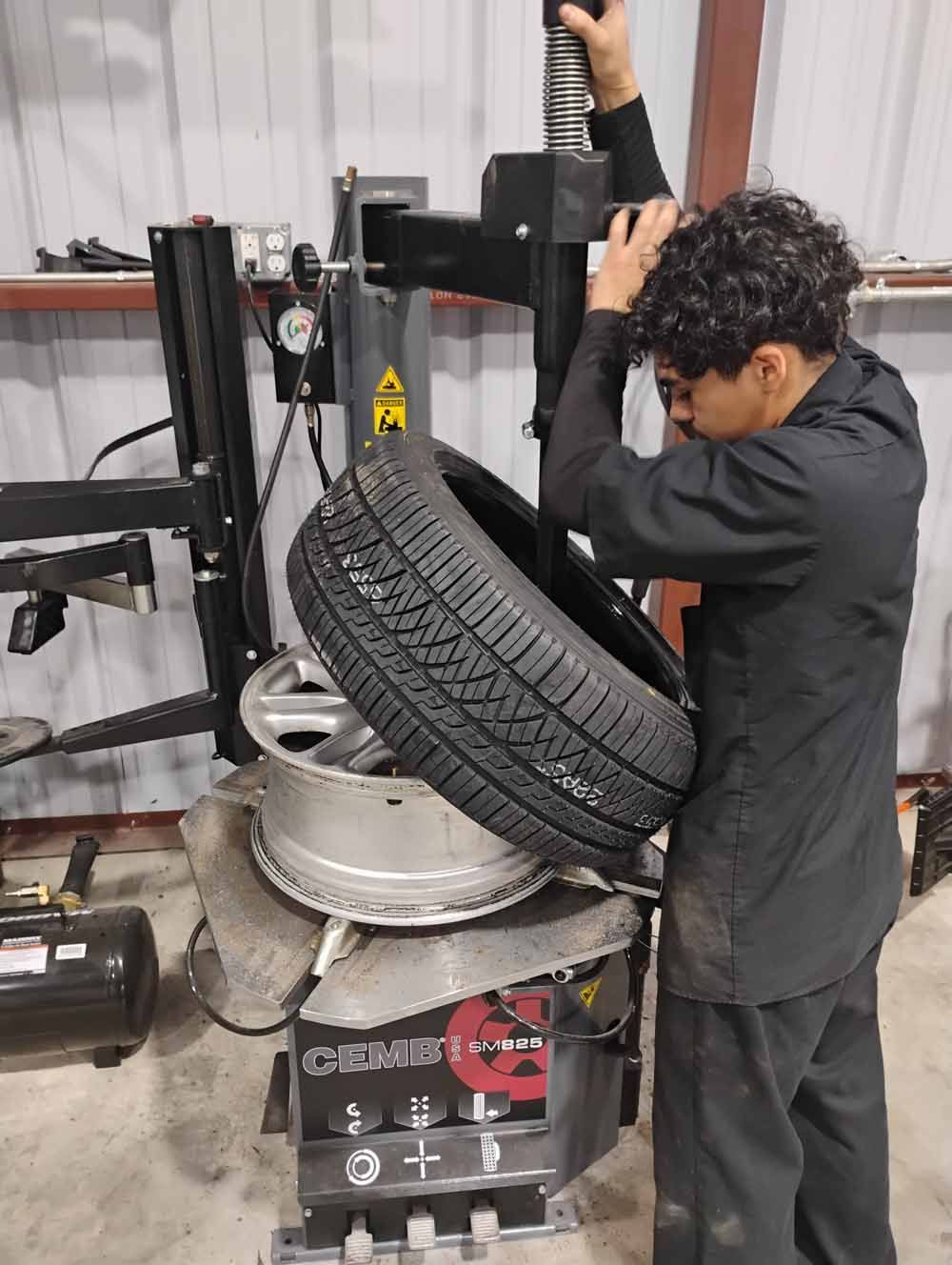 Mechanic using tire machine to remove tire from rim in a workshop.