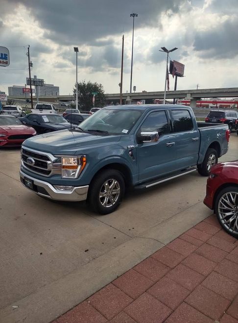 Blue Ford F-150 pickup truck parked at a car dealership. Chrome accents, cloudy sky.
