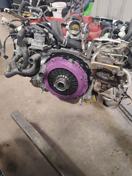 Engine with purple clutch installed. Mechanical parts, hoses, and wires visible in a shop setting.