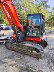 Orange and black excavator on a gravel surface. It is parked, with its arm extended upwards.